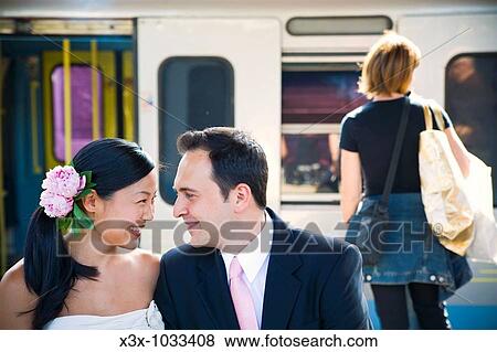 Stock Photo - Happy multi-ethnic bride and groom looking at each other in train station. Fotosearch