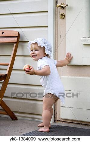 Happy One Year Old Baby Girl Standing Outside by Wooden Door with Apple in Hand View Large Photo Image Stock Photo - Happy One Year Old Baby Girl Standing Outside by Wooden Door with Apple in Hand. Fotosearch