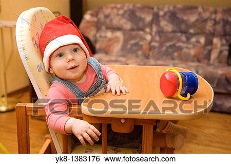 Stock Photograph - Happy Smiling Eight Month Old Infant Girl with Cup and Christmas Red Hat in High Chair. Fotosearch
