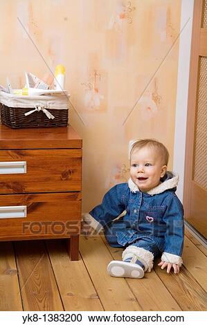 Stock Image - Happy Smiling Ten Month Old Baby Sitting on Floor by Bedside Tabel. Fotosearch