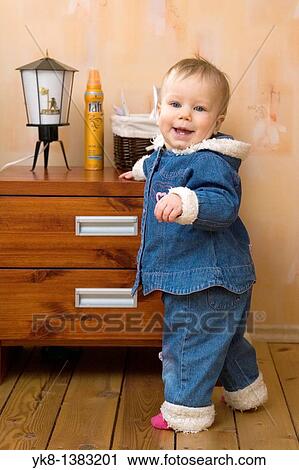 Stock Image - Happy Smiling Ten Month Old Baby Standing on Floor by Bedside Tabel. Fotosearch