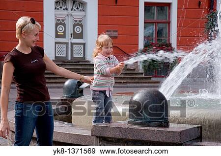 Stock Photo - happy smiling young woman and kid girl by fountain. Fotosearch
