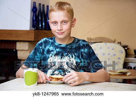 Stock Photography - Happy Teenage Boy Eating Breakfest Sandwich in Kitchen. Fotosearch