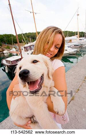 Stock Image - Happy young blond girl is holding her pet dog. Fotosearch