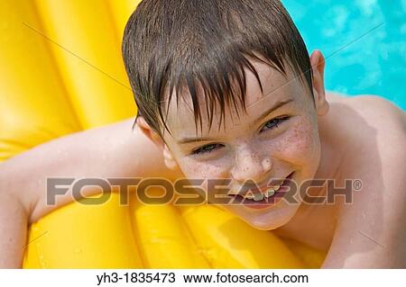 Happy young boy relaxing at the swimming pool on a yellow lilo View Large Photo Image Stock Image - Happy young boy relaxing at the swimming pool on a yellow lilo. Fotosearch