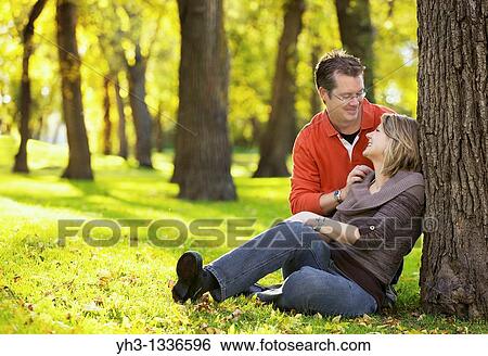 Stock Photograph - Happy young couple sitting at the park, looking at each other lovingly. Fotosearch