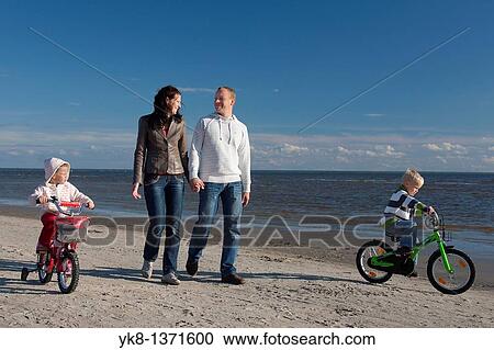 Stock Image - Happy Young Family Holding Hands Walking with Kids on Bicycles by Sea, P? rnu Beach, Estonia. Fotosearch