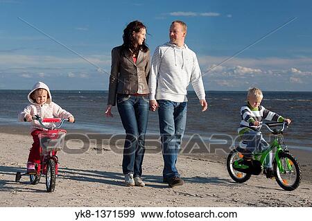 Happy Young Family Holding Hands Walking with Kids on Bicycles by Sea, P? rnu Beach, Estonia View Large Photo Image Stock Photo - Happy Young Family Holding Hands Walking with Kids on Bicycles by Sea, P? rnu Beach, Estonia. Fotosearch