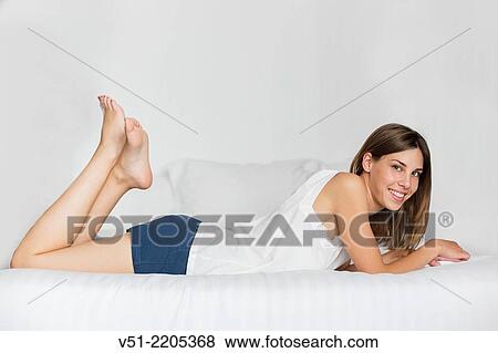 Stock Photo - Happy young woman smiling at camera and lying in bed. Fotosearch