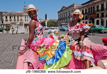Stock Photo - Havana Cuba local women with flowers at Capital in pink Classic Ford auto and hats smiling for tourists.. Fotosearch