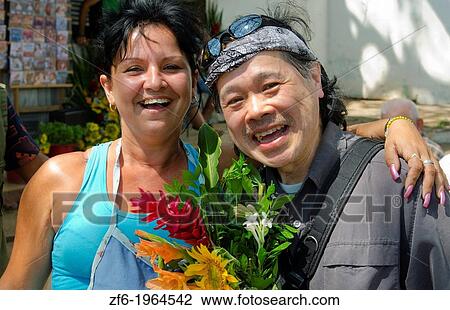 Stock Image - Havana Cuba woman selling flowers in market to Chinese tourist and smiling.. Fotosearch