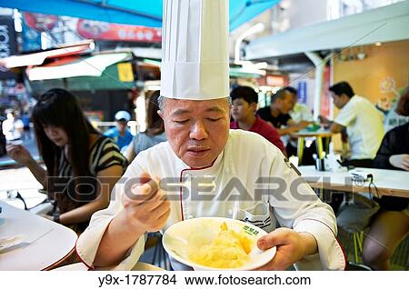 Picture - Head Chef Huang Lai Fa of The Grand Formosa Regent Hotel Taipei, posing and sampling food on Yongkang Street in Taipei, Taiwan. Fotosearch