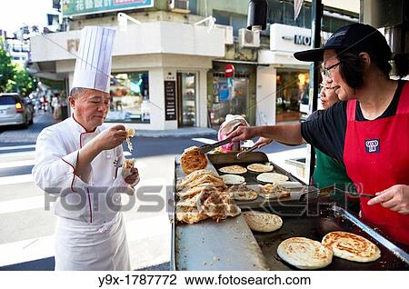 Stock Image - Head Chef Huang Lai Fa of The Grand Formosa Regent Hotel Taipei, posing and sampling food on Yongkang Street in Taipei, Taiwan. Fotosearch
