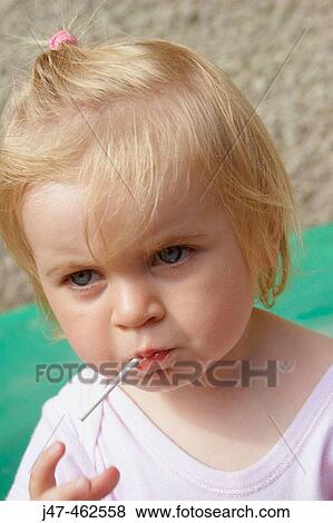 Stock Photo - Headshot of a 1 year old girl stanging outside in the sunshine eating a lolly. Fotosearch