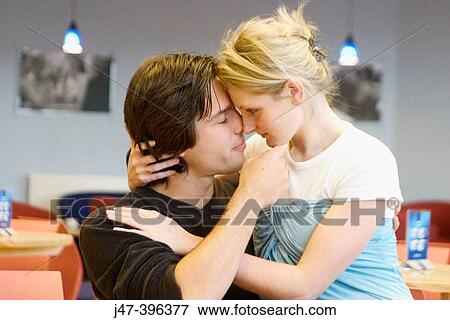 Stock Photo - Headshot of a young couple sitting in a cafe cuddling, she? s sitting on his knee, heads and noses together. Fotosearch