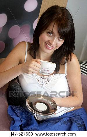 Stock Image - Headshot of a young girl sitting with a cup of coffee smiling into camera. Fotosearch