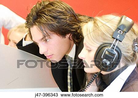 Stock Image - Headshot of a young man and lady at work on a computer, she's wearing headphones. Fotosearch