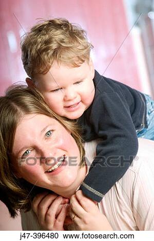 Stock Image - Headshot of woman 35, smiling into camera with 18 month old baby on her shoulders. Fotosearch