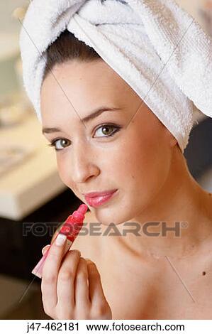 Stock Image - headshot of younge girl smiling into camera about to apply lipgloss wearing a towel on her head. Fotosearch