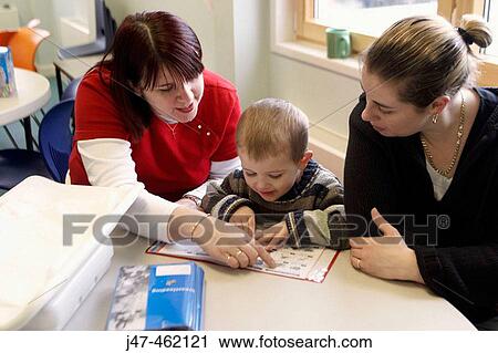 Stock Image - Health visitor showing 3 year old boy and his mother, a book. Fotosearch