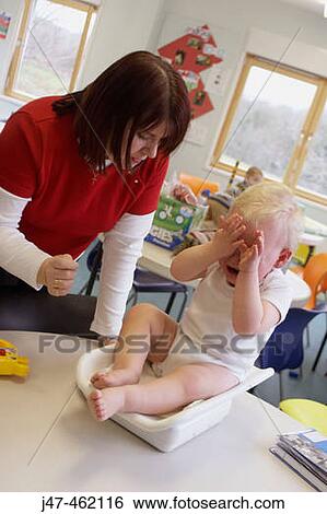 Stock Photograph - Health visitor weighing baby boy on the scales in a clinic. Fotosearch