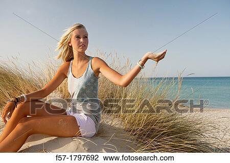 Healthy young woman sitting in the dunes letting sand flow through her fingers View Large Photo Image Stock Image - Healthy young woman sitting in the dunes letting sand flow through her fingers. Fotosearch