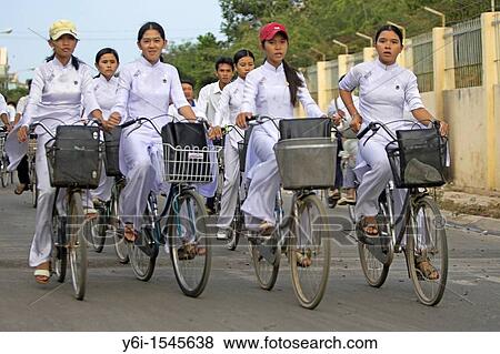 Stock Photo - High school girls in traditional white ao dai uniform ride home with school bags in bicycle baskets Phan Thiet Vietnam. Fotosearch