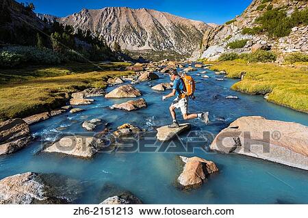 Stock Image - Hiker crossing stream in Sam Mack Meadow, John Muir Wilderness, Sierra Nevada Mountains, California USA.. Fotosearch
