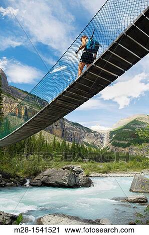 Stock Image - Hiker crossing suspension bridge on the Berg Lake Trail, Mount Robson Provincial Park British Columbia Canada. Fotosearch
