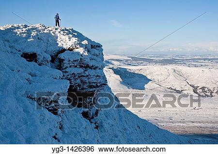 Stock Photograph - Hiker enjoys scenic winter view from summit of Corn Du, Brecon Beacons national park, Wales. Fotosearch