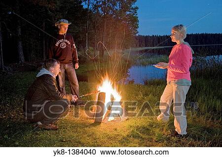 Stock Image - Hikers Companion by Campfire near Water in Night. Fotosearch