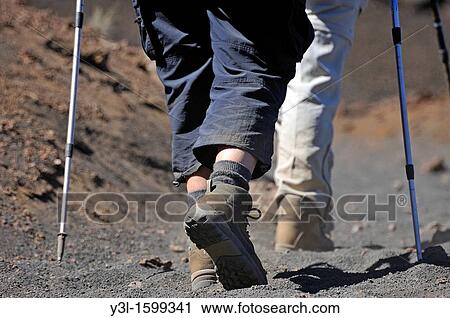 Stock Image - Hikers legs and sticks on volcanic trail, Haleakala crater, Maui Island, Hawaii Islands, USA. Fotosearch