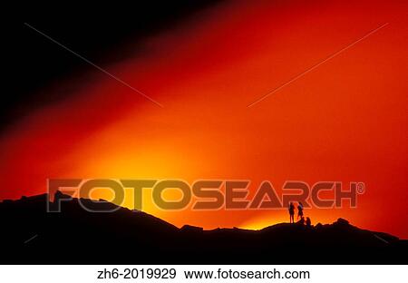 Stock Photo - Hikers watching lava flow enter the Pacific Ocean at night, Hawaii Volcanoes National Park, The Big Island, Hawaii USA.. Fotosearch