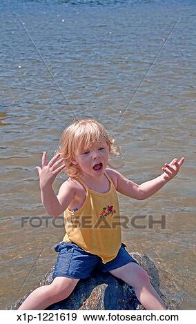 his young Caucasian girl is thoroughly enjoying a summer moment as she's sitting on a rock in a lake and singing her little heart out, complete with hands up in expression emotion Background water intentionally blurred to emphasize subject View Large Photo Image Stock Photo - his young Caucasian girl is thoroughly enjoying a summer moment as she's sitting on a rock in a lake and singing her little heart out, complete with hands up in expression emotion Background water intentionally blurred to emphasize subject. Fotosearch