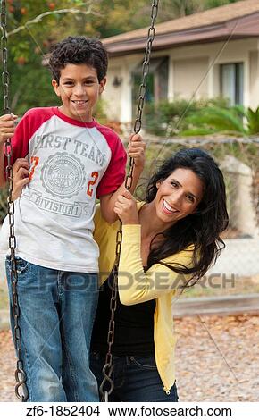 Hispanic single mother and som age 11 on swing in park at playground near home outdoors View Large Photo Image Picture - Hispanic single mother and som age 11 on swing in park at playground near home outdoors. Fotosearch