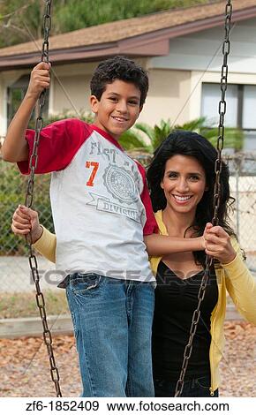 Hispanic single mother and som age 11 on swing in park at playground near home outdoors View Large Photo Image Stock Photo - Hispanic single mother and som age 11 on swing in park at playground near home outdoors. Fotosearch