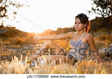 Stock Image - Hispanic teenage girl listening to music in nature around golden hour sunset. Fotosearch