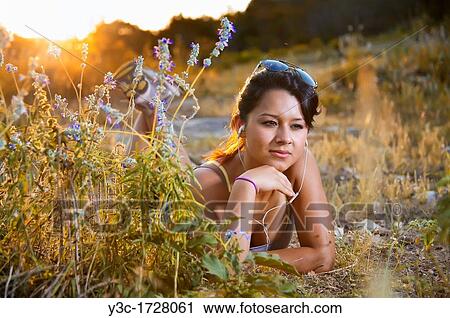 Stock Image - Hispanic teenage girl listening to music in nature around golden hour sunset. Fotosearch