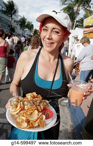 Stock Photo - Hispanic woman, drink, food, potato chips. Art Deco Weekend, Ocean Drive. Miami Beach. Florida. USA.. Fotosearch