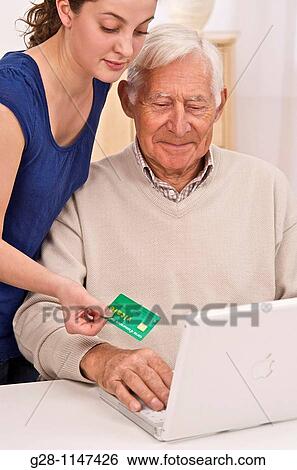 Home help or grand daughter holding green health card and helping senior man or grandfather with his computer View Large Photo Image Stock Photograph - Home help or grand daughter holding green health card and helping senior man or grandfather with his computer. Fotosearch