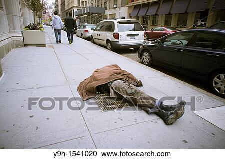 Stock Image - Homeless man sleeping on a vent in the sidewalk in Greenwich Village in New York With the deteriorating economy many worry about the return of crime and homelessness. Fotosearch