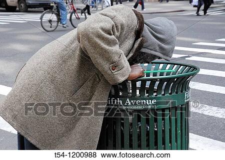 Stock Photo - Homeless person looking in a bin at the 5th Avenue recyclable materials. Fotosearch