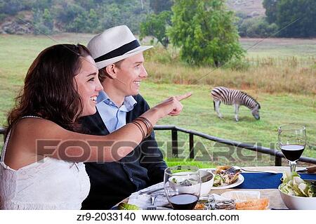 Honeymooning couple in late twenties eating picnic lunch outdoors with zebras in background, Winelands, Western Cape, Stellenbosch, South Africa. View Large Photo Image Stock Image - Honeymooning couple in late twenties eating picnic lunch outdoors with zebras in background, Winelands, Western Cape, Stellenbosch, South Africa.. Fotosearch
