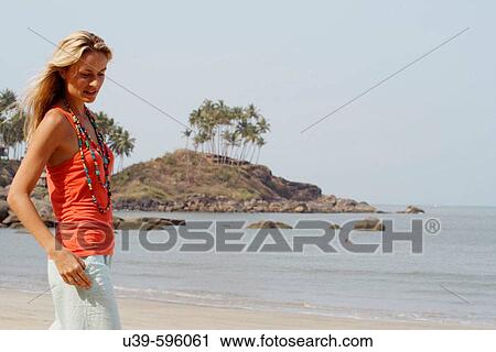Stock Image - Horizontal shot of a beautiful blonde woman wearing an orange vest and smiling on a beach in India.. Fotosearch