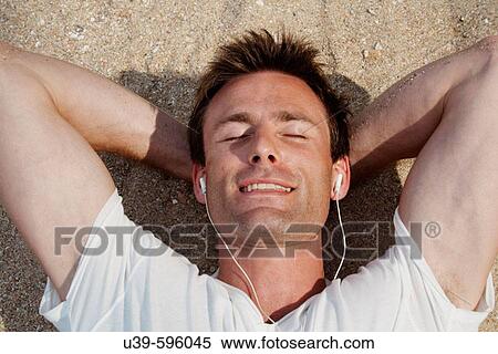 Horizontal shot of a god-looking man lying on the beach in India and listening to headphones with his eyes closed. View Large Photo Image Stock Photography - Horizontal shot of a god-looking man lying on the beach in India and listening to headphones with his eyes closed.. Fotosearch