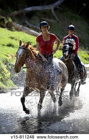 Stock Photo - horseriders cantering through river. Fotosearch