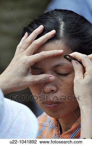 Stock Image - Hue (Vietnam): a woman cutting another woman's eyebrows with a razor blade at the Dong Ba market. Fotosearch