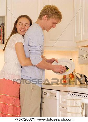 Stock Image - hugging her man while he does the dishes. Fotosearch