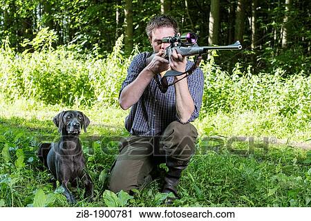 Stock Image - Hunter with dog, aiming with rifle with telescopic sight. Fotosearch