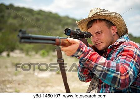 Hunting season in America - Man with cowboy hat shooting a rifle View Large Photo Image Stock Photo - Hunting season in America - Man with cowboy hat shooting a rifle. Fotosearch